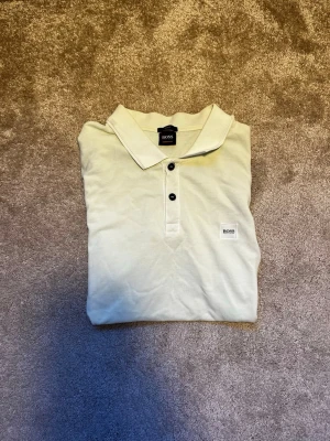 Ljusgrön slim fit piké från Hugo Boss - Snygg ljusgrön piké från Hugo Boss i slim fit-modell. Skjortan har klassisk krage, tre svarta knappar framtill och en diskret BOSS-logga på bröstet. Tillverkad i 100% bomull för skön känsla och stilren look. Priset ej hugget i sten hör av er vid frågor eller funderingar! 