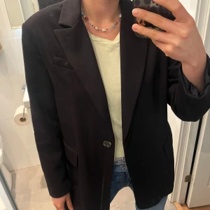 Svart kavaj med klassisk passform - Säljer en svart kavaj med klassisk krage och enkel knappstängning framtill. Kavajen har två fickor med lock och en bröstficka, samt långärmade ärmar. Passar till jeans eller kostymbyxor.