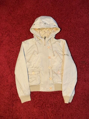 Abercrombie & Fitch Bomber jacka - Abercrombie and Fitch bomber jacka i storlek M. Den är liten i storleken. Den har knappar på luvan för att det ska sitta en päls där men den saknas tyvärr, kanske går att hitta någonstans. Mått: axelbredd - 43 cm, längd - 51 cm. Skriv för fler bilder och frågor!