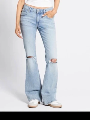 Bootcut jeans med slitna knän - Bootcut jeans  i ljusblå tvätt med slitna detaljer vid knäna. Modellen har klassisk femficksdesign och låg midja. Jeansen är tillverkade i mjukt denim och har en avslappnad passform med utsvängda ben. Perfekta för dig som gillar en chill och trendig stil.