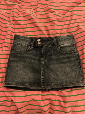  jeanskjol från H&M Divided - Säljer en svart jeanskjol från H&M Divided med dubbla silverknappar och dragkedja fram. Kjolen är kort och har en rak passform med snygga kontrastsömmar. Perfekt för sommarn🫰