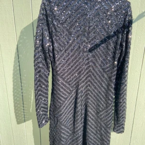 Svart glittrig paljettklänning - Säljer en svart kortklänning med långa ärmar och rund hals. Klänningen är täckt av glittriga paljetter i ett chevronmönster som ger en riktigt snygg effekt. Perfekt för dig som vill sticka ut och glänsa på nästa fest eller event.mycket bra skick använd 1 gång, hämtas i NORSBORG Botkyrka eller fraktas. sitter mycket elegant på . Passar L-XL är lite stretch.