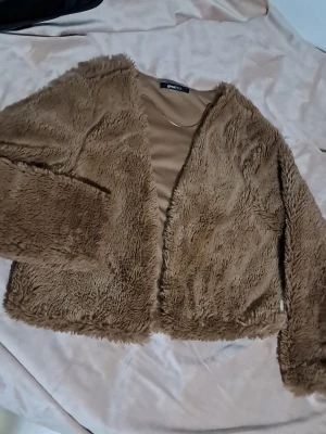 Beige pälsjacka från Gina Tricot - Säljer en fluffig och mjuk beige pälsjacka från Gina Tricot. Jackan har långärmade ärmar, öppen framtill och är i en loose passform. Perfekt för dig som vill ha en cozy vibe och gillar att sticka ut med en trendig look.