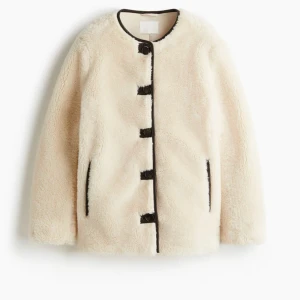 Beige teddyjacka med svarta detaljer - Säljer en  beige teddyjacka med svarta knappar och svarta detaljer vid fickor och kanter. Jackan har rund halsringning och långa ärmar, perfekt för dig som vill ha en mysig och trendig look. Nypris 549, lappen kvar, helt slutsåld💗