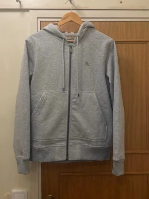 Burberry hoodie  - Grå Burberry kofta som håller dig varm och stilfull hela vintern. Tillverkad i mjukt, högkvalitativt material med klassiska Burberry detaljer som gör den både skön att bära och enkel att matcha.