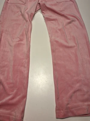 Rosa mjukisbyxor från Juicy Couture - Säljer ett par klassiska rosa mjukisbyxor från Juicy Couture. Byxorna är i mjuk velour med raka ben och resår i midjan. Perfekta för chill dagar eller när du vill ha en avslappnad look. Ikonisk LA-vibe och superbekväma!