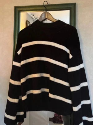 Svartvit randig stickad tröja - Säljer en svart stickad tröja med breda vita ränder. Tröjan har en rund hals och långa ärmar med loose passform. Perfekt för dig som gillar en chill och avslappnad stil. Materialet är mjukt och ger en skön känsla mot huden.