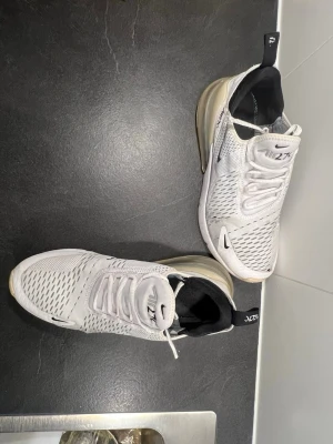 Nike skor  - Nike Air Max 270 sneakers i vit färg med svarta detaljer och synlig luftkudde i hälen. Ovandelen är tillverkad i ventilerande syntetmaterial med mesh och har snörning. Snygg och modern design med rund tå och platt sula, perfekt för dig som gillar streetstyle. Tveka inte på prisförslag.Dom är stretchiga och passar även för dom som har storlek 42  och 43. Använda ett par gånger men inget stort hål som ni ser på bilderna 