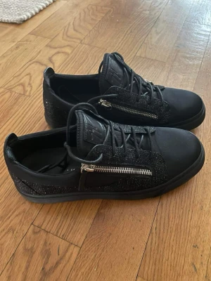 Guiseppe Zanotti skor svart  - Säljer ett par svarta skor från Giuseppe Zanotti med glittriga detaljer och silverfärgade dragkedjor på sidorna. Nypris 7,500 sek