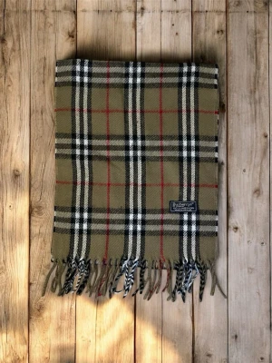 Burberry halsduk - Säljer en klassisk rutig halsduk från Burberry i beige, svart, vit och röd. Halsduken är tillverkad i 100% lammull. Halsduken är perfekt nu under vintern för att kunna hålla sig varm och stilren. Tveka inte att höra av dig vid frågor eller funderingar.