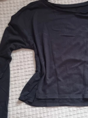 Svart långärmad träningströja Energetics - Svart långärmad träningströja från Energetics med meshpaneler på sidorna för extra ventilation. Tröjan har rund hals och är tillverkad i ett lätt syntetmaterial som andas. Perfekt för gymmet eller löprundan.