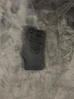 Svarta Replay Anbass jeans - Snygga svarta Replay Anbass jeans med smal passform och klassisk femficksdesign. Jeansen har en mörk tvätt och subtila detaljer vid fickorna. Perfekta för dig som gillar stilrena och moderna jeans med lite edge.