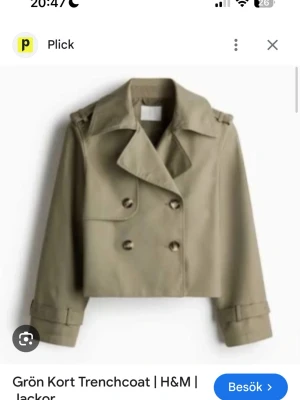 Grön croppad trenchcoat från H&M - Snygg grön croppad trenchcoat från H&M med dubbelknäppning och klassisk krage. Jackan har långa ärmar med spänndetaljer vid mudden och axelklaffar. Perfekt för dig som vill ha en trendig och stilren look. Passar xs-s