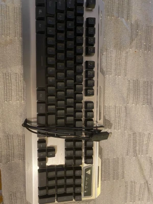  Gaming Keyboard - Robust gamingtangentbord med metallram och USB-anslutning. Fullstort med numerisk del och funktionsknappar. Tangenterna ser hela ut och tangentbordet är i gott skick, med mindre tecken på användning. Perfekt för gaming eller kontorsbruk.