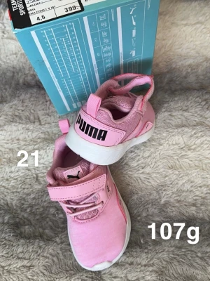 Rosa sneakers från Puma strl 21 - Säljer ett par söta rosa Puma sneakers i storlek 21. Skorna har vit sula, elastiska snören och kardborreband för enkel påtagning. Ovandelen är i mesh och syntetmaterial, med stor Puma-logga bak. Perfekta för små fötter som vill springa runt!🌸 Nya. Skickas utan kartong. Stl 21