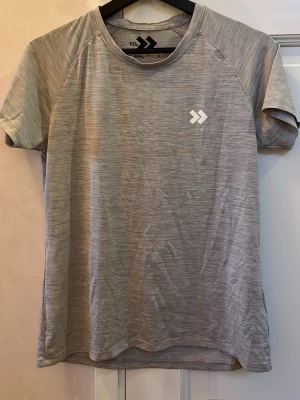 Grå t-shirt från 157, storlek S - Säljer en grå t-shirt från 157 i storlek S. T-shirten har korta ärmar, rund hals och ett diskret mönster med tunna linjer. Materialet känns lätt och andas bra, perfekt för träning eller chill. Loggan sitter snyggt på bröstet.