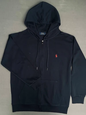 Mörkblå hoodie från polo Ralph lauren  - Snygg mörkblå tröja med dragkedja från polo Ralph lauren och en röd broderad logga på framsidan. Bra skick endast testat på en gång 