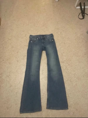 Blå bootcut jeans från DIVIDED - Snygga blå bootcut jeans från DIVIDED, storlek 32. Klassisk femficksmodell med knapp och dragkedja fram. Jeansen har en lätt tvättad look och är tillverkade i jeansmaterial som ger en skön känsla. Perfekt för dig som gillar retrovibbar och vill ha ett par jeans med lite extra sväng i benen.