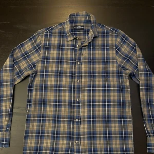 Rutig blå skjorta från Hampton Republic - Säljer en snygg rutig skjorta från Hampton Republic i regular fit, storlek S. Skjortan har en klassisk krage, knappar framtill och långärmade ärmar. Färgerna är blå, beige och grå.