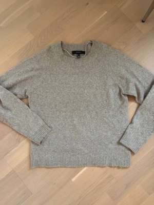 Beige/brun stickad tröja  - Säljer en beige stickad tröja  med rund hals och långa ärmar. Tröjan har ribbade muddar vid ärmslut och nederkant, perfekt för att hålla värmen under kyliga dagar. Enkel och stilren design som funkar till många olika outfits.