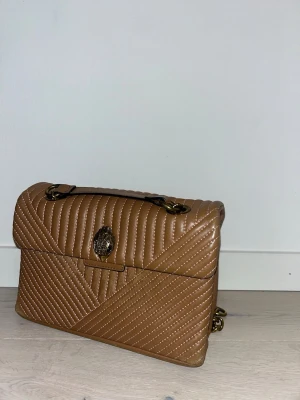 Quiltad brun axelväska från Kurt Geiger - Snyggaste väskan från Kurt geiger! Älskar gulddetaljerna! Liten sliten vid kanterna samt under kurt märket. Tyvärr behöver den ett nytt hem 🙇🏼‍♀️
