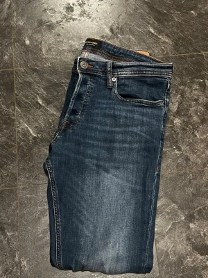 Mörkblå skinny jeans från Jack & Jones - Säljer ett par mörkblå skinny jeans från Jack & Jones. Klassisk femficksmodell med snygga slitningar och kontrastsömmar. Jeansen har normal midja och smal passform hela vägen ner. Perfekta till sneakers och hoodie.