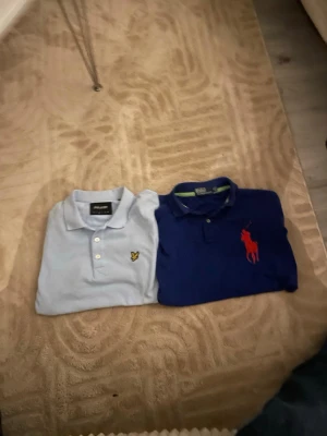Två pikétröjor Lyle & Scott och Polo Ralph Lauren - Säljer två snygga pikétröjor i storlek S. En ljusblå från Lyle & Scott med gul logga på bröstet och klassisk krage med knappar. Den andra är marinblå från Polo Ralph Lauren med röd stor logga på bröstet och krage med knappar. Perfekt till jeans eller shorts.