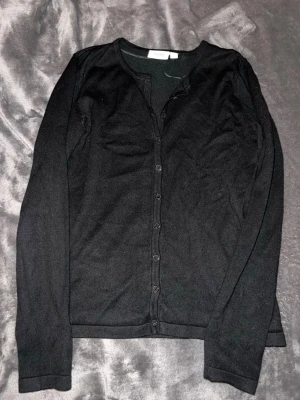 Svart kofta med knappar - Svart, klassisk kofta från Saint Tropez med knappar hela vägen framtill! Långärmad och i mjukt, tunt stickat material som sitter snyggt på kroppen💕