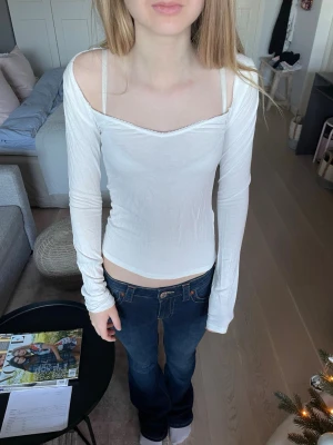 Vit långärmad topp från Nelly XS - Säljer en vit långärmad topp från Nelly i storlek XS. Toppen har en smal passform, offshoulder-skärning och söt spetskant längs urringningen. Materialet är mjukt och stretchigt, perfekt till jeans eller kjol.