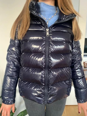 Glansig Colmar Down Jacket- Dunjacka - Säljer denna super snygga glansiga, mörkblåa vinterjackan ifrån Colmar. Jackan har en klassisk quiltad design med ett tydlig Colmar märke på vänster ärm! Den har även hög krage och justerbara spännen längst ner vilket är perfekt inför kalla dagar. Den är sparsamt använd under två vintrar så är i fint skick!💞