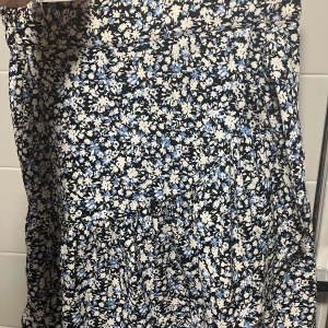 Blommig kjol från Lindex - Säljer en kjol från Lindex i storlek S med blommigt mönster. Kjolen har resår i midjan för skön passform och volang nertill.