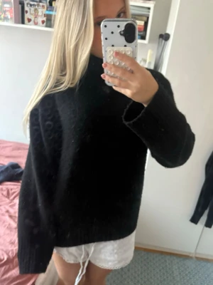 Svart stickad polo oversized tröja - Mysig svart stickad tröja med hög hals och långa ärmar. Modellen är oversized och har en enkel, stilren design utan synliga detaljer. Perfekt att slänga på sig när det är kyligt ute.