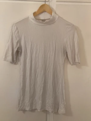 Vit ribbad polotopp från RCHLO - Säljer en enkel och stilren vit polotopp från RCHLO Basics. Toppen är ribbad med korta ärmar och har en hög krage som ger en clean look. Perfekt att matcha med jeans eller kjol för en avslappnad vibe.