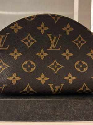 Sminkväska  - Sminkväska med guldiga detaljer och dragkedja. Halvmåneformad design. Perfekt för att organisera dina sminkprodukter och borstar.