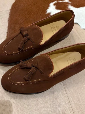 Myrqvist Mölle bruna loafers  - Säljer ett par stilrena bruna loafers från Myrqvist, modell Mölle. Skorna är tillverkade i mjuk mocka med dekorativa tofsar framtill och har en klassisk rund tå. Snygga kontrastsömmar och lädersula ger en exklusiv känsla. Perfekta för dig som gillar tidlös design och kvalitet.