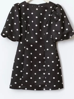 Svart prickig kortklänning med puffärm - Supersöt svart kortklänning med vita prickar och puffiga korta ärmar. Klänningen har en figurnära passform och är sydd i ett glansigt material som ger en lyxig känsla. Perfekt för dig som vill sticka ut med ett klassiskt men trendigt mönster.