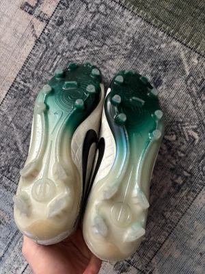 Nike tiempo vita fotbollsskor - Säljer ett par Nike Mercurial fotbollsskor i vitt med grönt Nike-märke och detaljer. Skorna har snörning, quiltad ovandel och platt sula med dobbar för gräsplan. Materialet är syntet och mesh, och insidan är blå. Perfekt för dig som vill ha snygga och funktionella skor på planen. Lite smutsiga men annars inga problem 