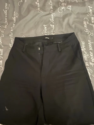 Svarta kostymbyxor från Bik Bok - Svarta kostymbyxor från Bik Bok i storlek 34. Klassisk rak passform med hällor för bälte, diskreta fickor bak och fram samt dragkedja och knappstängning. Materialet känns mjukt och har en stilren look som funkar till många olika outfits.