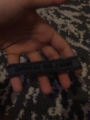 Mörkblå Christian Dior J'Adior armband - Säljer ett snyggt mörkblått armband från Christian Dior med texten 'J'Adior' broderad i svart. Armbandet är gjort i ett slitstarkt tygmaterial och har en enkel, stilren design som passar perfekt till din outfit.