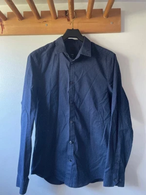 Mörkblå prickig skjorta med knappar - Snygg mörkblå skjorta med små vita prickar och klassisk krage. 