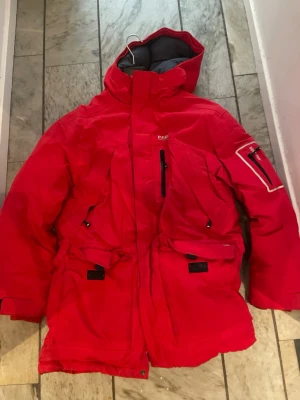 Röd vinterjacka Peak Performance - Peak Performance röd dunjacka stl M expedition parka i Gore Tex. Peak Performance Expedition Parka är en robust dunparkas framtagen för sträng vinterkyla och nyckfullt väder. Den funkar lika bra på fjällturen som på stan. Jackan har en skyddande huva, tvåvägsdragkedja framtill med stormslå samt justerbara ärmslut med kardborre och mjuka innermuddar. Flera framfickor, ärmficka och innerfickor. Midja och nederkant med dragsko kan justeras. 
