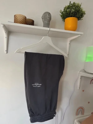 Mörkgrå mjukisbyxor med dragkedja - Snygga mörkgrå mjukisbyxor med tryck på benet och praktisk dragkedja vid benslutet. Byxorna har elastisk mudd och är gjorda i mjukt material som känns skönt mot huden. Perfekta för chill eller träning, med en modern och avslappnad look.