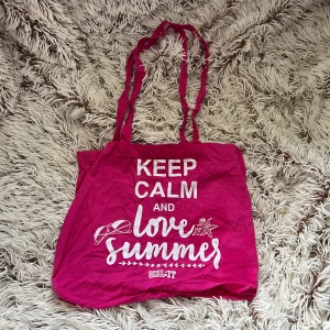 Rosa tygväska från GIRL:IT - Säljer en rosa shoppingväska från GIRL:IT med texten 'KEEP CALM AND love summer' i vitt framtill. Väskan har långa axelband och är gjord i mjuk bomull, perfekt för att bära med sig allt man behöver under sommaren.  Tyvärr har den lite lösa trådar vid handtagen 