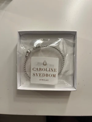 Silverfärgad kristallarmband Caroline Svedbom - Snyggt armband från Caroline Svedbom i silverfärgad metall. Aldrig använd eller testad och i sin orginalförpackning oöppnad. Säljer då jag fick 2 likadana i julklapp. Pris kan ej diskuteras. Original pris 795kr.