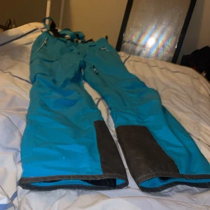 Turkosa täckbyxor från Everest - Säljer ett par turkosa täckbyxor från Everest med svarta förstärkningar vid bensluten och hängslen. Byxorna har flera dragkedjeförsedda fickor och justerbara detaljer. Perfekta för vinterns äventyr och outdoor-aktiviteter.Är som storlek xs