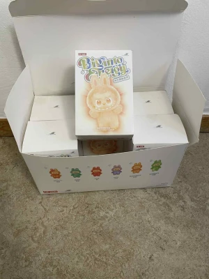 Ingen väst på bilderna - Bilderna visar en låda med Pop Mart Big Into Energy samlarfigurer, inte en väst. Ingen information om väst, färg, form, märke eller material kan identifieras.