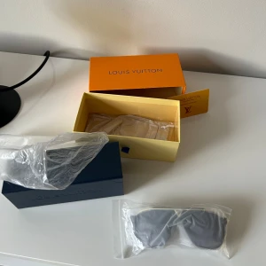 Svarta Louis Vuitton solglasögon - Säljer ett par svarta solglasögon från Louis Vuitton med klassisk, stilren design. Glasögonen har breda bågar och mörka glas, levereras med originalbox och tillbehör. Perfekta för dig som vill ha en lyxig och trendig accessoar.
