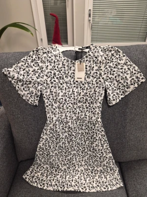 Bik Bok DK Willow vit och svart klänning, storlek XS - Supersöt vit kortklänning från Bik Bok med svart blommigt mönster. Klänningen har korta ärmar, rund hals och en snygg öppen ryggdetalj. Tillverkad i återvunnen polyester med ett mjukt foder. Perfekt för dig som gillar romantisk stil och vill sticka ut.