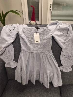 Bik Bok DW Air grå klänning, storlek XS - Supersöt ljusgrå klänning från Bik Bok i storlek XS. Klänningen har långärmade puffärmar med broderade detaljer och smockad överdel. Kjolen är volangig och ger en flowy känsla. Materialet är mjukt och känns som bomull, perfekt för dig som gillar romantisk stil.