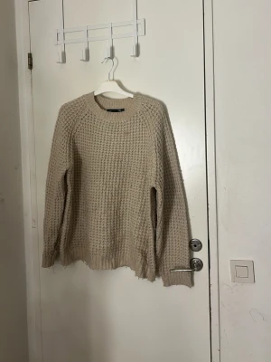 Beige stickad tröja  - Säljer en beige stickad tröja, strukturerad yta och rund hals. Tröjan har långa ärmar och ribbade muddar vid hals, ärmslut och nederkant. Perfekt för lager-på-lager under kyliga dagar. Pris kan diskuteras och tvätt ingår innan leverans 